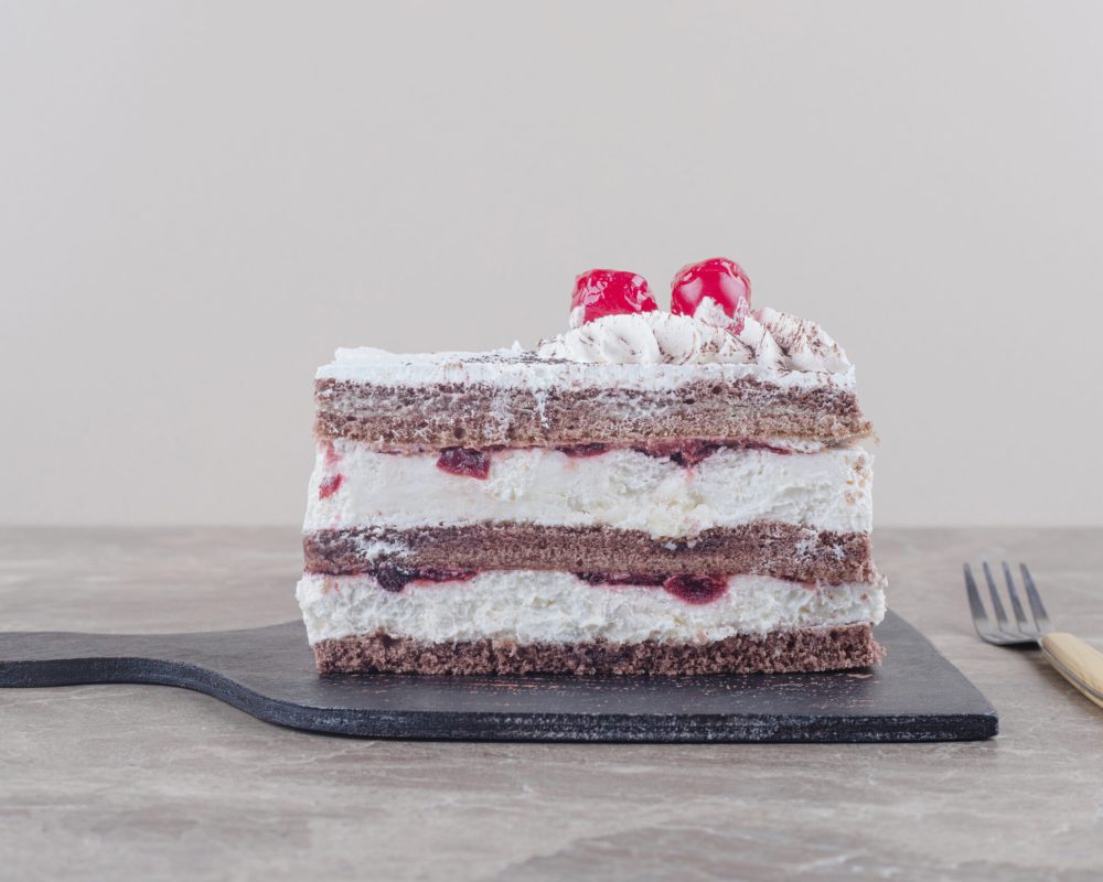 Small cake slice with cream, cherry and cocoa powder topping on a board on marble background. High quality photo